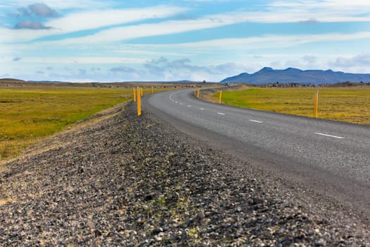 Highway through Icelandic landscape under a blue summer sky with clouds
