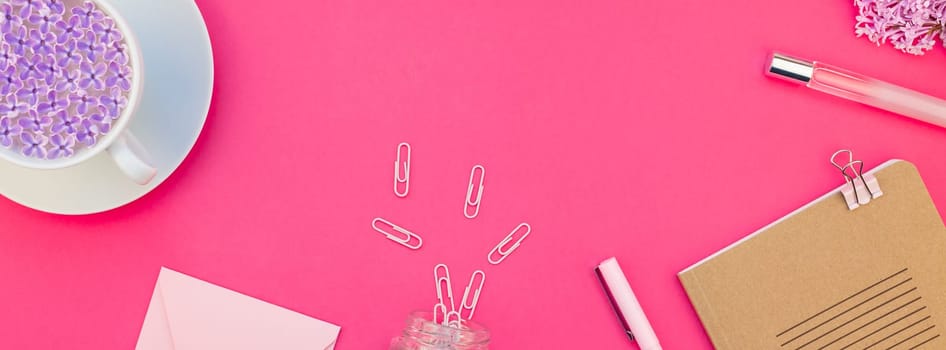Creative top view flat lay of workspace desk styled design office supplies and cup of tea with copy space on a bright pink color paper long wide banner. Template for feminine blog social media