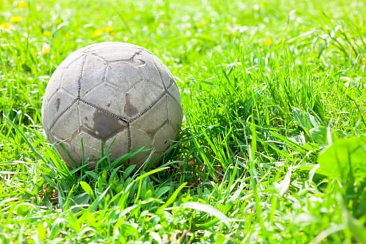 Old soccer ball forgotten in the green grass field. The football concept