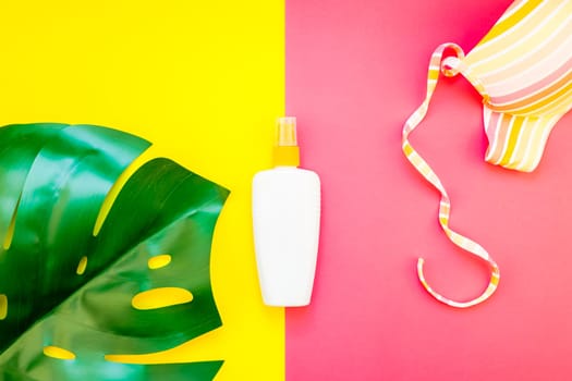 Tropical jungle palm monstera leaves, sunglasses, sunscreen blank bottle mockup and woman's swimsuit top on bright color paper background. Summer vacations creative flat lay concept template for text