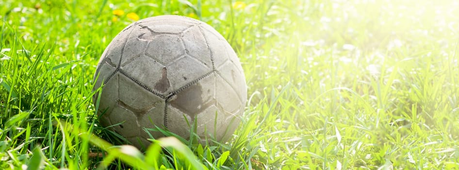 Old soccer ball forgotten in the green grass field. The football concept. Long wide banner