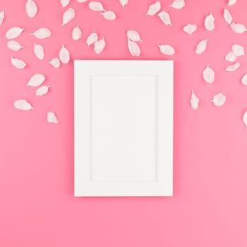 Creative flat lay concept top view of white frame mock up and apple tree flowers petals on square pastel pink background with copy space in minimal style, template for text