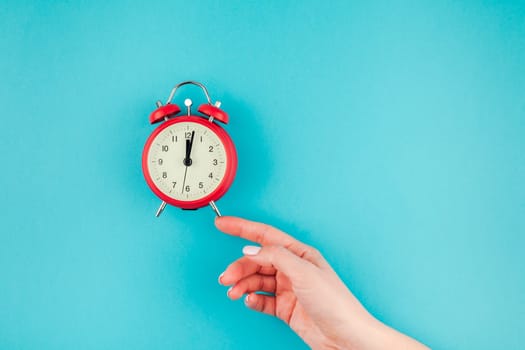 Creative flat lay concept top view of woman hand holding the red vintage alarm clock on bright blue turquoise color paper background with copy space in minimal style, template for text