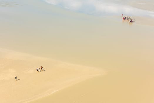 View from walls of Mont Saint Michel on the bay during the low tide with groups of tourists walking. France