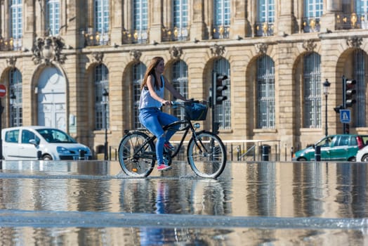 FRANCE, BORDEAUX - SEPTEMBER 20: People riding bicycles in the mirror fountain in front of Place de la Bourse in Bordeaux, France on September 20, 2015