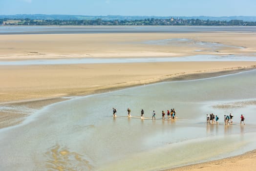 FRANCE, MONT SAINT MICHEL - SEPTEMBER 26: View from walls of Mont Saint Michel on the bay during the low tide with groups of tourists walking. France on September 26, 2015