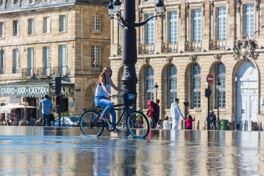 FRANCE, BORDEAUX - SEPTEMBER 20: People riding bicycles in the mirror fountain in front of Place de la Bourse in Bordeaux, France on September 20, 2015