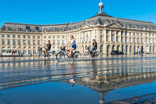 FRANCE, BORDEAUX - SEPTEMBER 20: People riding bicycles in the mirror fountain in front of Place de la Bourse in Bordeaux, France on September 20, 2015