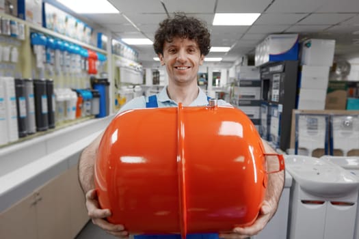 Portrait of male plumber carrying hydraulic tank or grease trap for sewage bought at plumbing shop