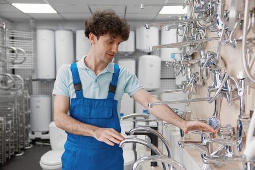 Male plumber selecting stainless steel washbasin water tap for domestic kitchen or home bathroom at plumbing store