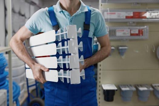 Crop view of plumber wearing uniform holding section of water heating radiator while shopping at plumbing store