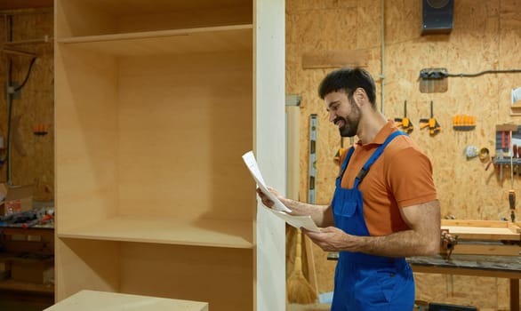 Carpenter looking at paper sheet with project blueprint reading assembly instructions standing over woodshop interior