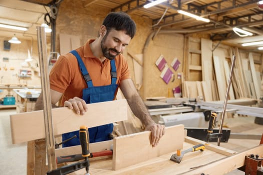 Male artisan worker holding and assembling pieces of wood using glue working at workbench. Craftsmanship and carpentry studio concept