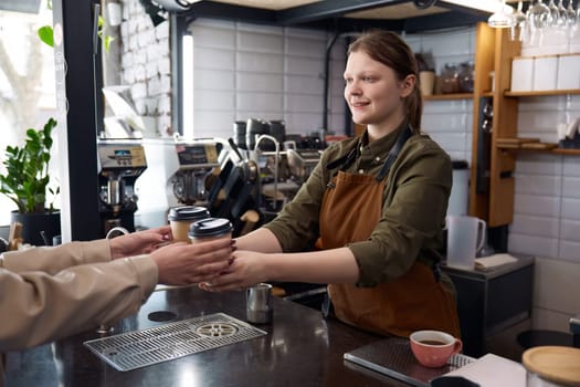 Female barista serving coffee in takeaway recycling paper cups. Female client receiving order at coffee-shop