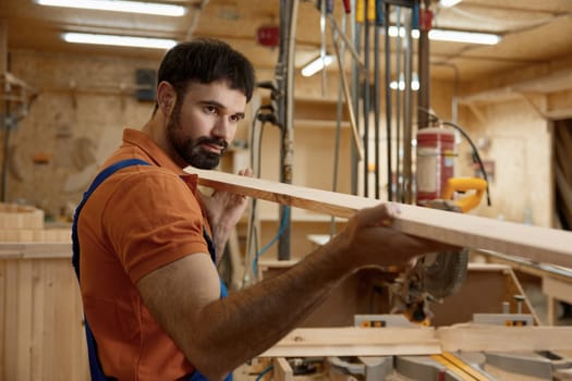 Portrait of artisan holding wooden timber checking plank straightness standing over woodwork studio background