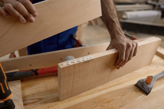 Male artisan worker holding and assembling pieces of wood using glue working at workbench. Craftsmanship and carpentry studio concept