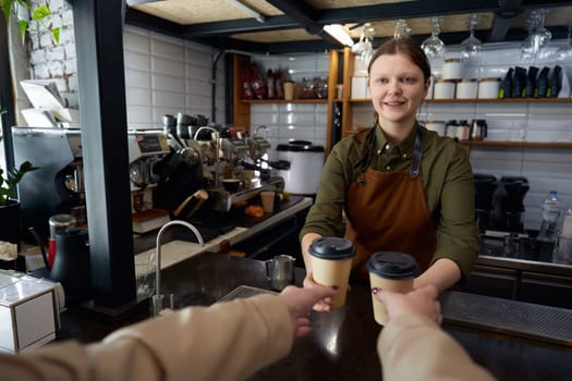 Female barista serving coffee in takeaway recycling paper cups. Female client receiving order at coffee-shop