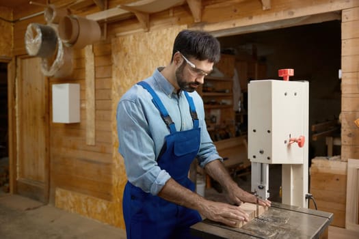 Carpentry shop worker processing woods at stationary electric jigsaw. Professional job occupation at furniture production manufactory