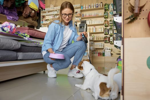 Young woman choosing new food bowl for her dog. Labrador dog enjoying shopping at pet store