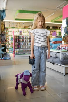 Portrait of sad little girl with toy dog on leash dreaming about real pet animal standing over pet store background