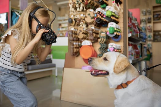 Cute little girl showing new muzzle for Labrador dog at pet shop. Family shopping activity on weekend