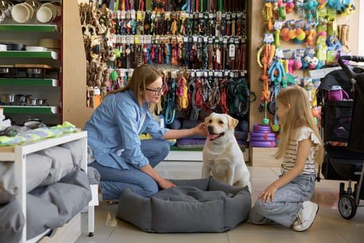 Happy mother and daughter choosing bed place for dog enjoying shopping at pet store