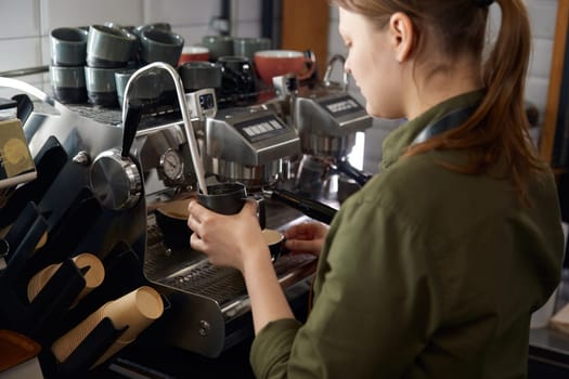 Portrait of woman barista cooking cappuccino on coffeemaker machine with frothing warm milk equipment. Coffee-shop service