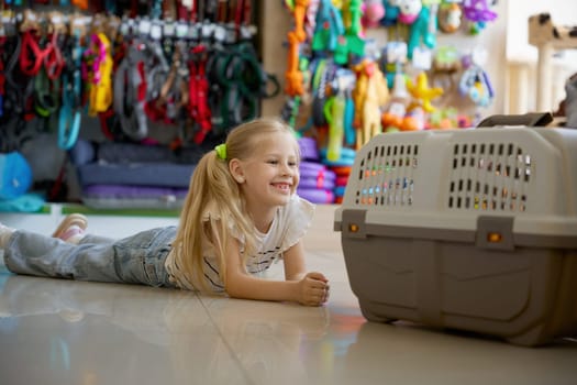 Cute smiling girl child lying on floor of pet shop looking inside doggy carriage. Professional service and great assortment of goods for domestic animals