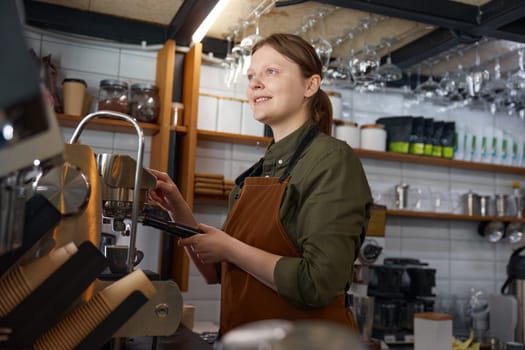Portrait of dreamy looking woman barista brewing coffee on coffeemaker machine. Professional restaurant appliance for high quality client service
