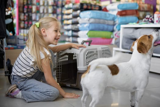 Little girl child calling dog to sit inside new plastic carriage bought at pet shop. Safety transportation for puppy assortment