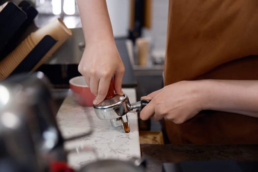 Cropped shot of woman barista making coffee on counter in cafe. Closeup view on female hands holding coffee-maker machine equipment. Food and drink service concept