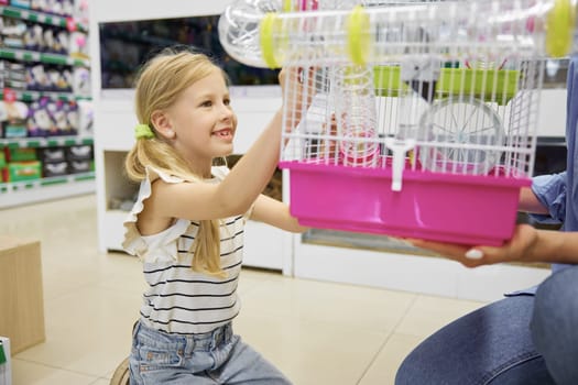 Cute daughter looking at new hamster cage in mother hands. Happy family shopping at pet store