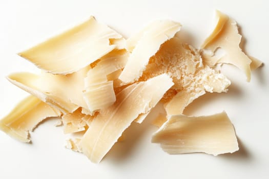 Delicate shavings of parmesan cheese arranged aesthetically on a clean white surface. The light highlights the varied textures and colors of the cheese, showcasing its rich, creamy nature.