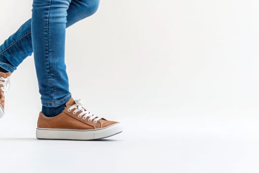 A person is captured mid-step, wearing casual brown sneakers and blue jeans, creating a dynamic and energetic vibe against a stark white backdrop.