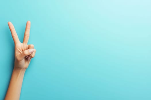 A hand displays a classic peace sign against a solid turquoise background, conveying a message of unity and positivity. The simplicity of the background highlights the gestures significance.