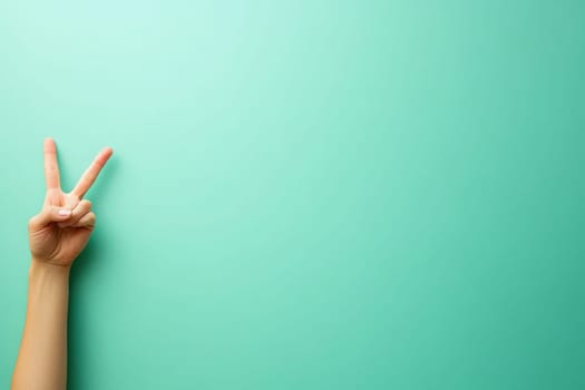 A hand is positioned to form a peace sign, standing out against a clean turquoise background. The simplicity of the gesture evokes feelings of tranquility and harmony.
