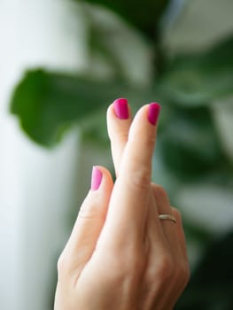 Female Hands With Purple Nails Manicure. Woman Fingernails With Pink Magenta Nails On Green Lush Background. Aesthetic Visual Of Trendy Manicure. Short Nails With Gel Or Nail Polish Lacquer
