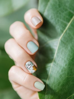 Female Hands With Different-Colored Nails. Fall Manicure. Woman Fingernails With Pastel Green and Taupe Colors Nails. Autumn Stamping Nail Art Design. Aesthetic Visual Of Fall Botanical Stamping