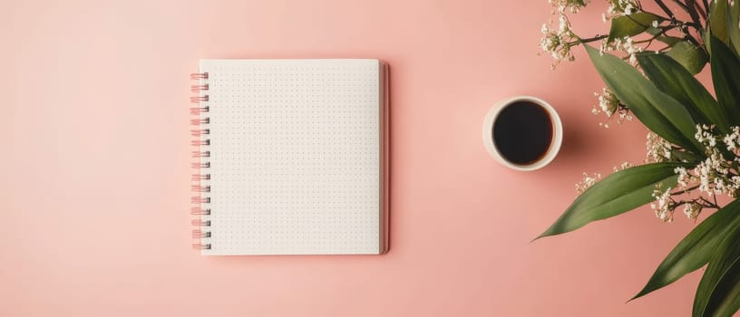 A spiral notebook and a cup of coffee on a pink background with floral accents, offering copy space.