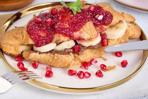 Croissant with chocolate, banana pieces and raspberry jam on a plate