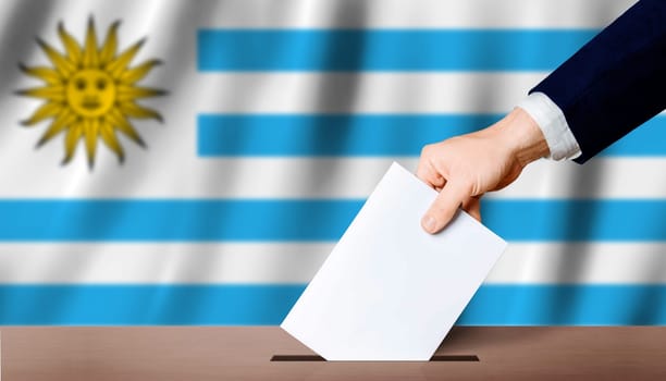 Uruguay Presidential elections. Hand holding ballot in voting ballot box with Uruguay flag in background