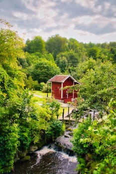 Stream with a small bridge in front of a red wooden house in Sweden. Trees on the bank . Scandinavian nature