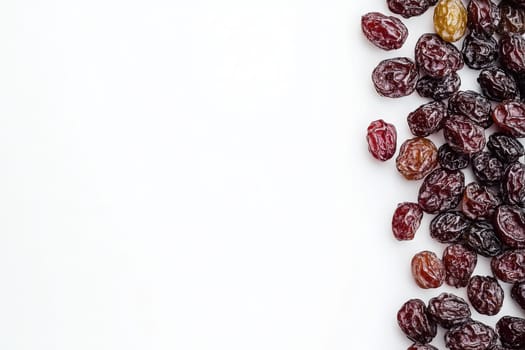 A variety of raisins are scattered on a spotless white surface, highlighting their rich colors and unique shapes. The assortment includes different types, showing natural appeal.