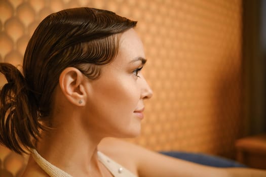 Side view of an elegant woman with her smooth hair tied back against a textured background