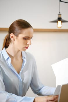 A woman in office intently reviewing documents in a modern environment, illuminated by natural light. Her concentration emphasizes the importance of her task.
