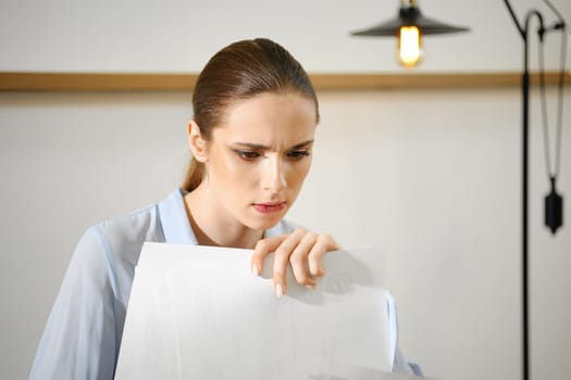 A woman looks worried while going through a stack of important documents in a well-lit office space