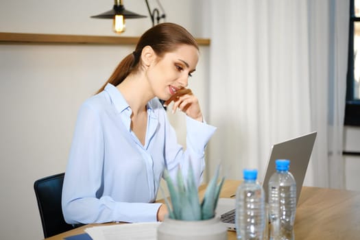 A woman sits at a stylish desk in a modern home office, concentrating intently on her laptop.