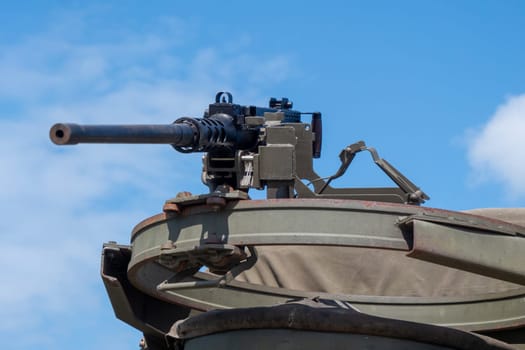 A machine gun is on a metal object with a green cover. The gun is pointed at the camera