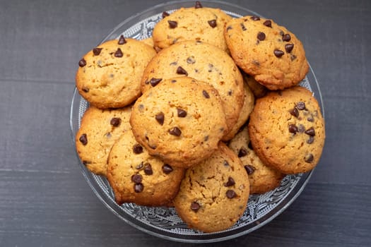A bowl of chocolate chip cookies with a lot of chocolate chips. The cookies are piled on top of each other, and the bowl is clear