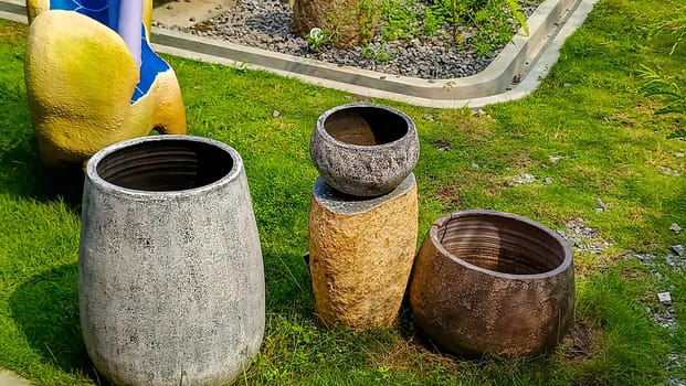 A vibrant outdoor scene featuring four decorative garden pots of various textures and colors, placed on a well-maintained lawn. A partial view of a yellow and blue artistic sculpture is visible too.